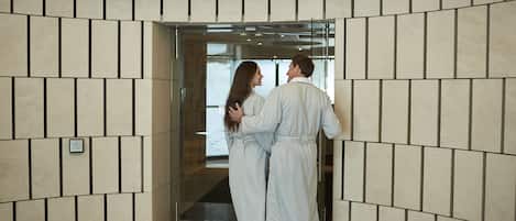 Una pareja parada frente a la entrada de un spa, con una pared de azulejos y un letrero arriba.