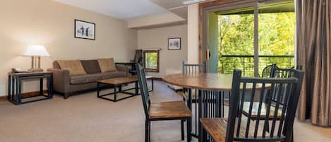 Un salon comprenant un canapé, des fauteuils, une table et une lampe. Les murs sont ornés de tableaux encadrés et il y a une fenêtre avec des rideaux.