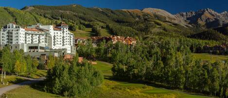 A hotel with multiple floors, surrounded by lush greenery and mountains.