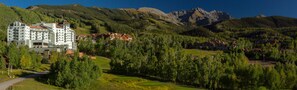 A hotel with multiple floors, surrounded by lush greenery and mountains.