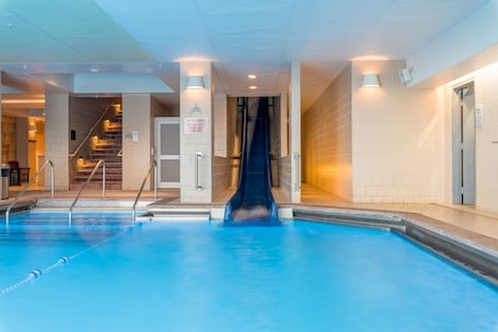 An indoor swimming pool with a slide, a staircase, and a sign indicating the slide is active.