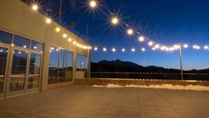 Un bâtiment doté de grandes portes et fenêtres en verre, d’un toit recouvert de tuiles et d’une guirlande de lumières se détachant sur le ciel nocturne.