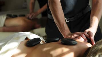 En massagebehandling där personen ligger på mage och får en ryggmassage med hjälp av stenar.