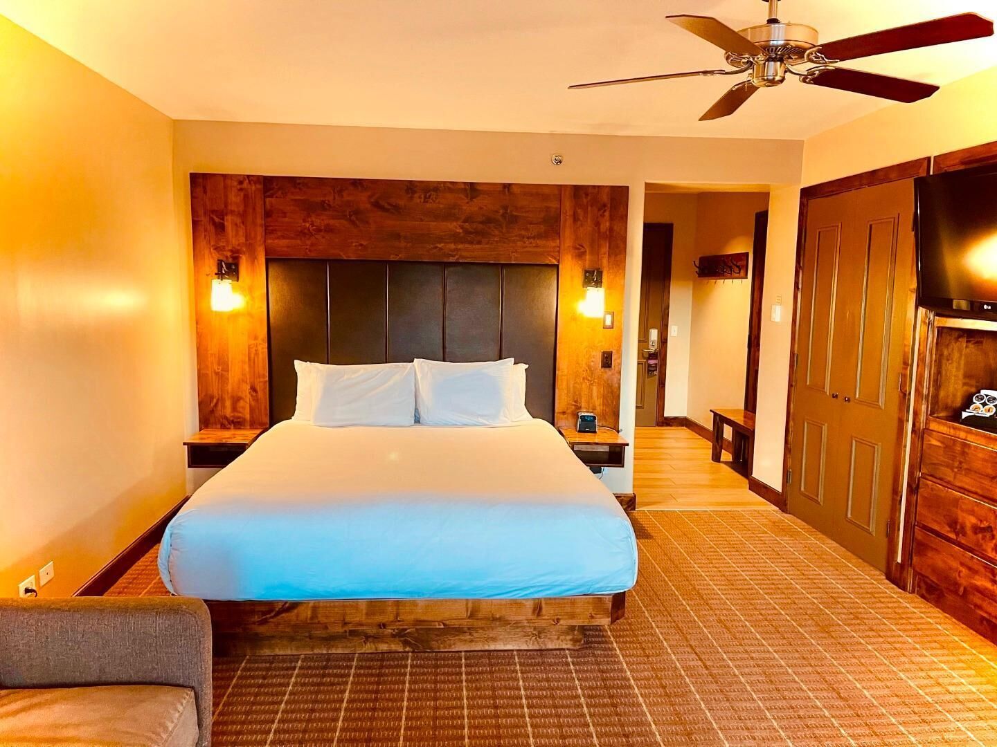 A hotel room with a bed, wooden headboard, nightstands, a television, and a ceiling fan.