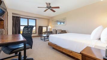 A hotel room with a bed, desk, office chair, and a ceiling fan.