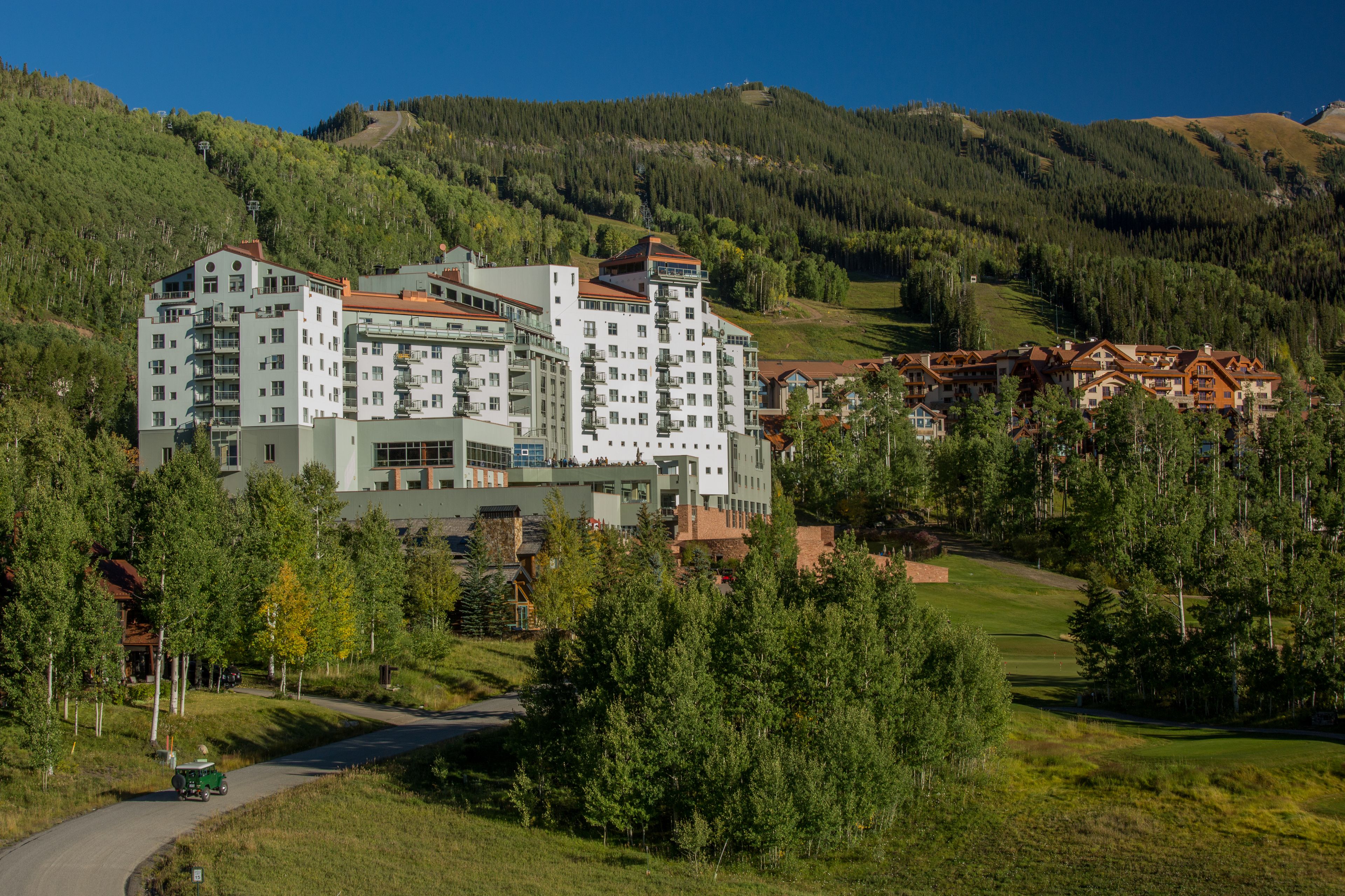 A multi-story hotel with a modern architectural design, surrounded by lush greenery and hills.