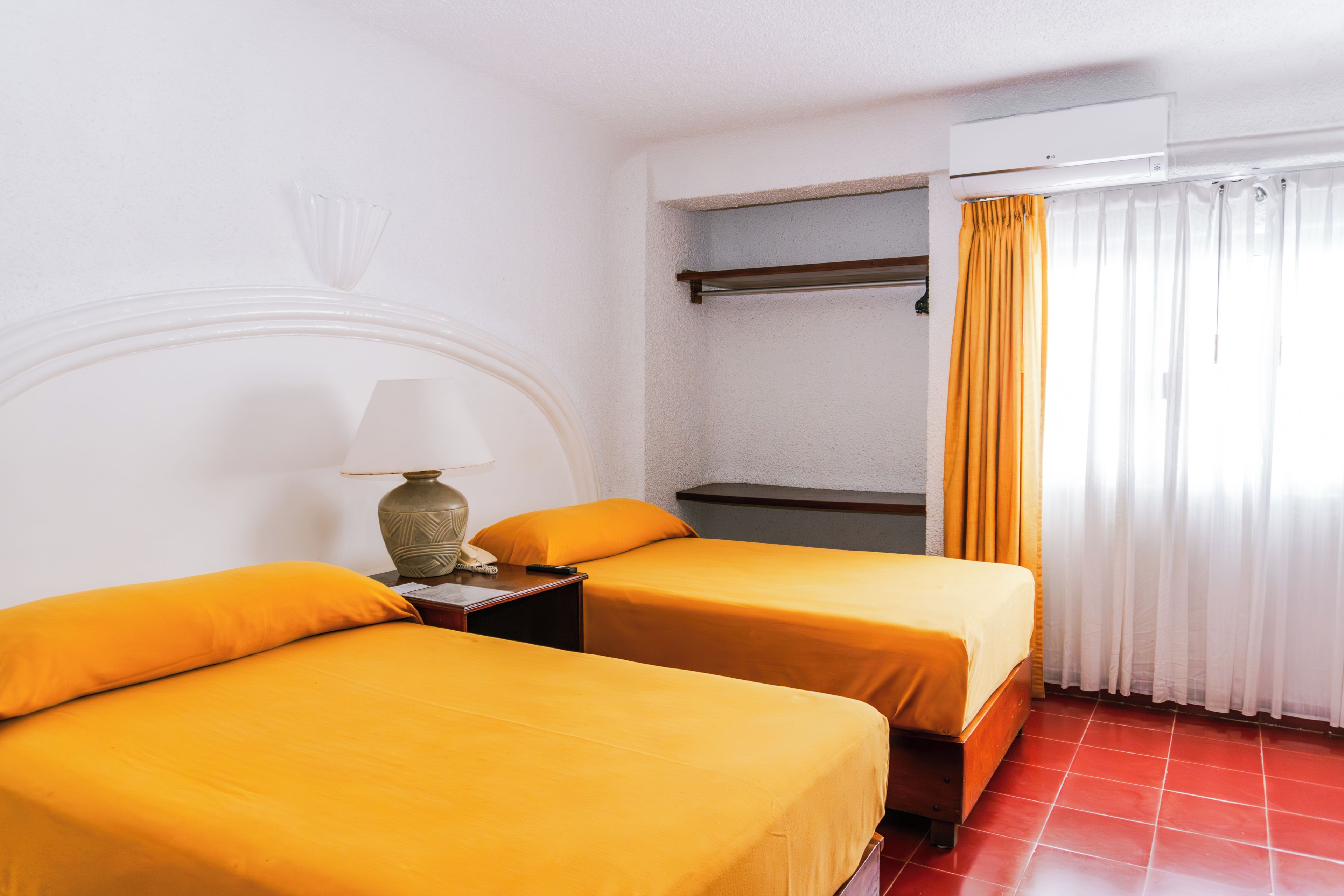 A hotel room with two beds, a nightstand with a lamp, a wardrobe, and a window with curtains.