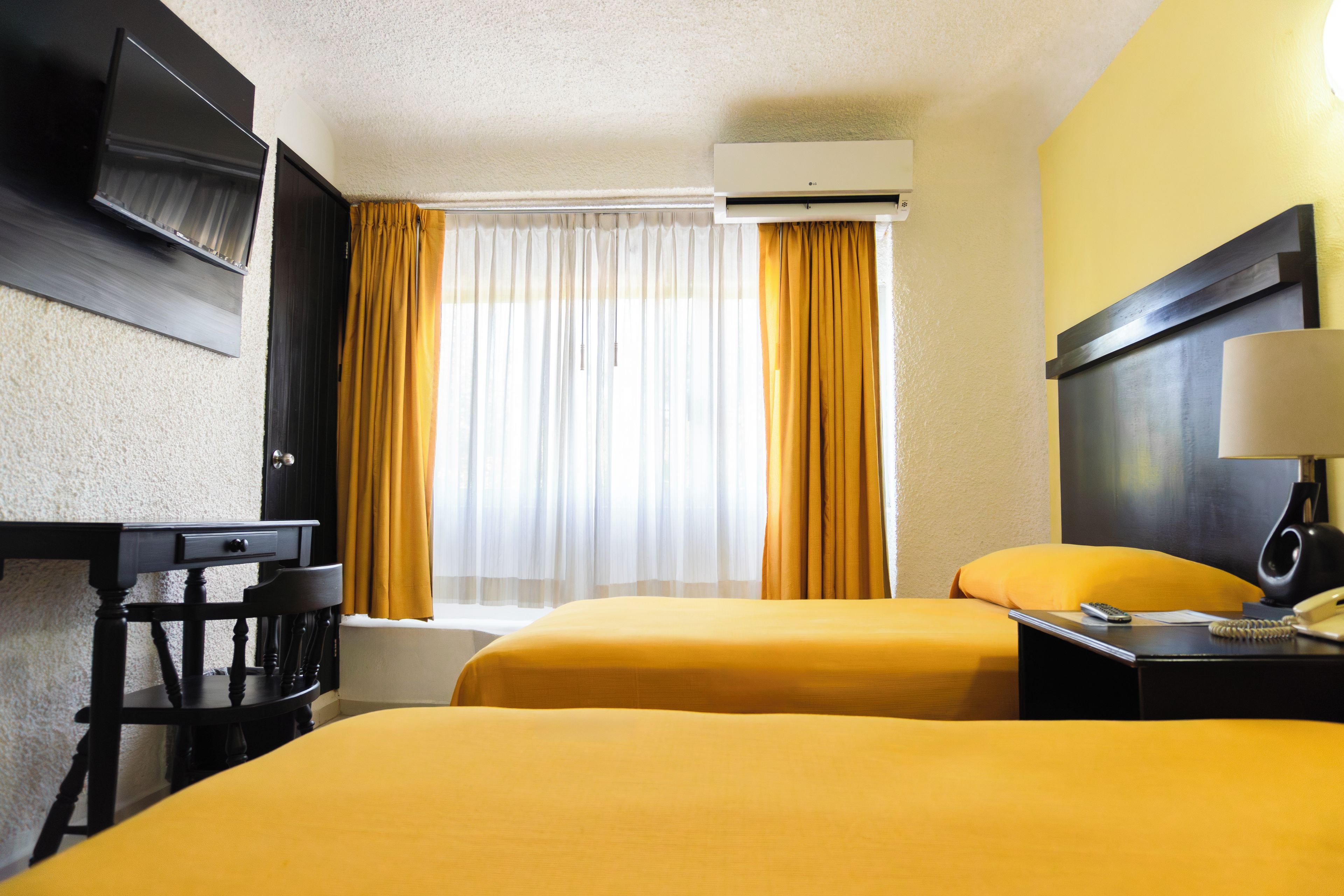 Une chambre d’hôtel avec deux lits, un bureau, une chaise, une télévision et une fenêtre avec des rideaux.