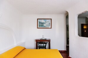 A room with a bed, a desk with a chair, a framed picture on the wall, and a door with a sign.