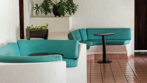 Un área de estar con sofás azul turquesa y blancos, una mesita redonda y plantas en macetas sobre una pared blanca.