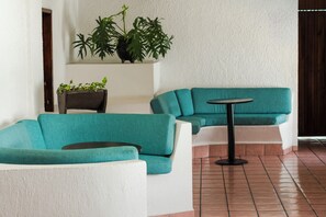 Eine Sitzecke mit SalbeigrĂŒn- und weiĂen Sofas, einem kleinen runden Tisch und Blumentöpfen an einer weiĂen Wand.