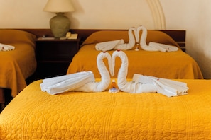 A hotel room with two beds, each with a yellow quilted bedspread and white towels arranged in a swan shape.