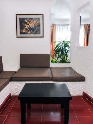 A room with a sofa, a table, a framed picture, and a window with curtains.
