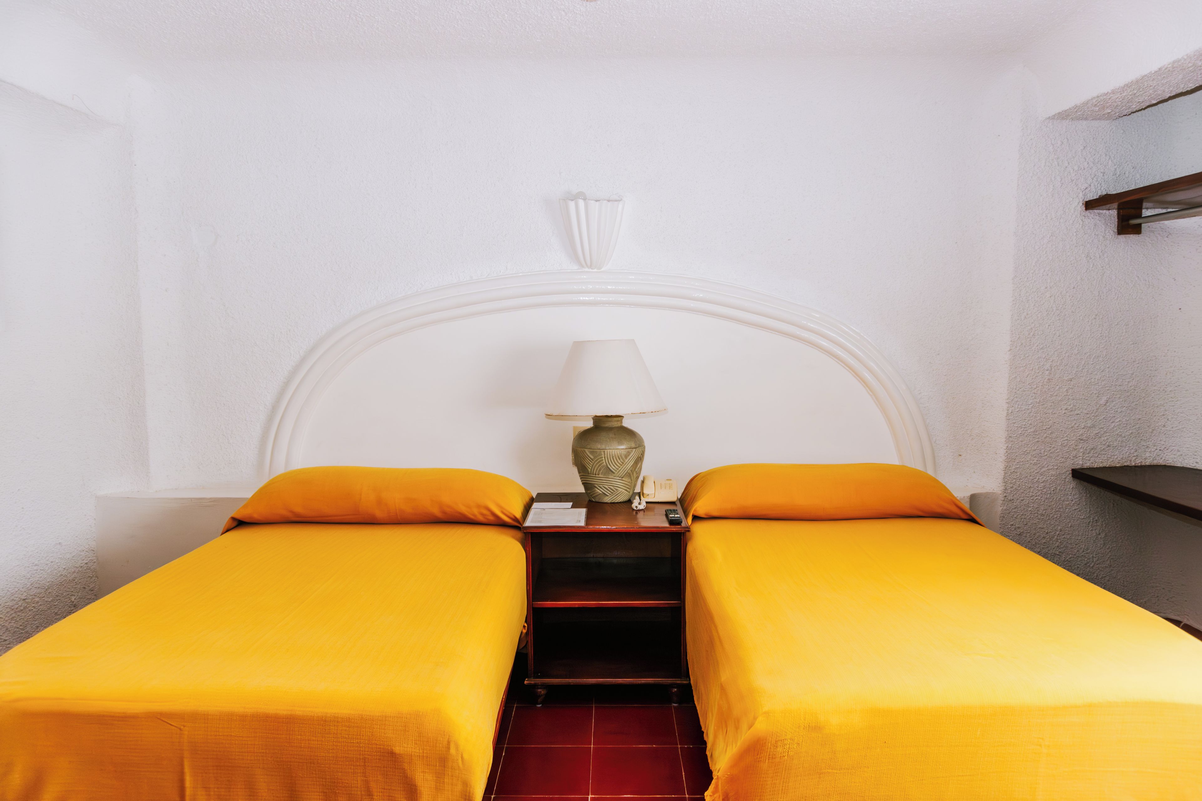 Une chambre avec deux lits, une table de chevet avec une lampe et une petite étagère.