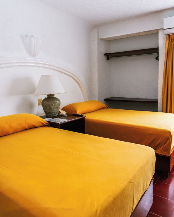Habitación de hotel con dos camas, una mesita de noche con lámpara, teléfono y una ventana con cortinas.