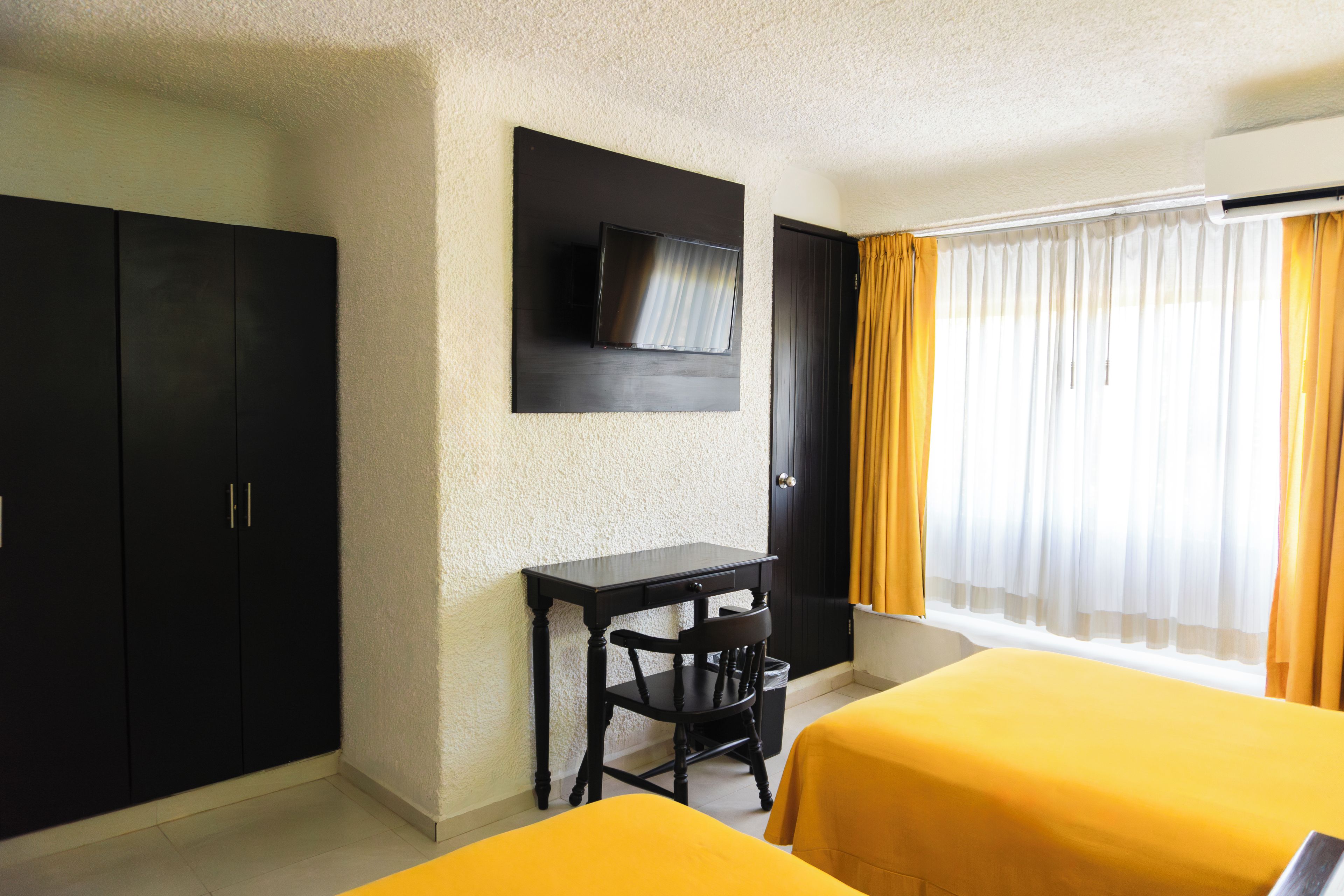 A hotel room with two beds, a desk, a chair, a TV, and a wardrobe.