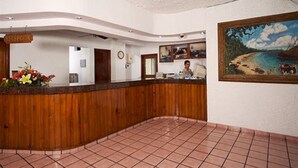 Un espace d’accueil avec un comptoir de réception en bois, une enseigne indiquant « Réception » et un tableau représentant une scène de plage accroché au mur.