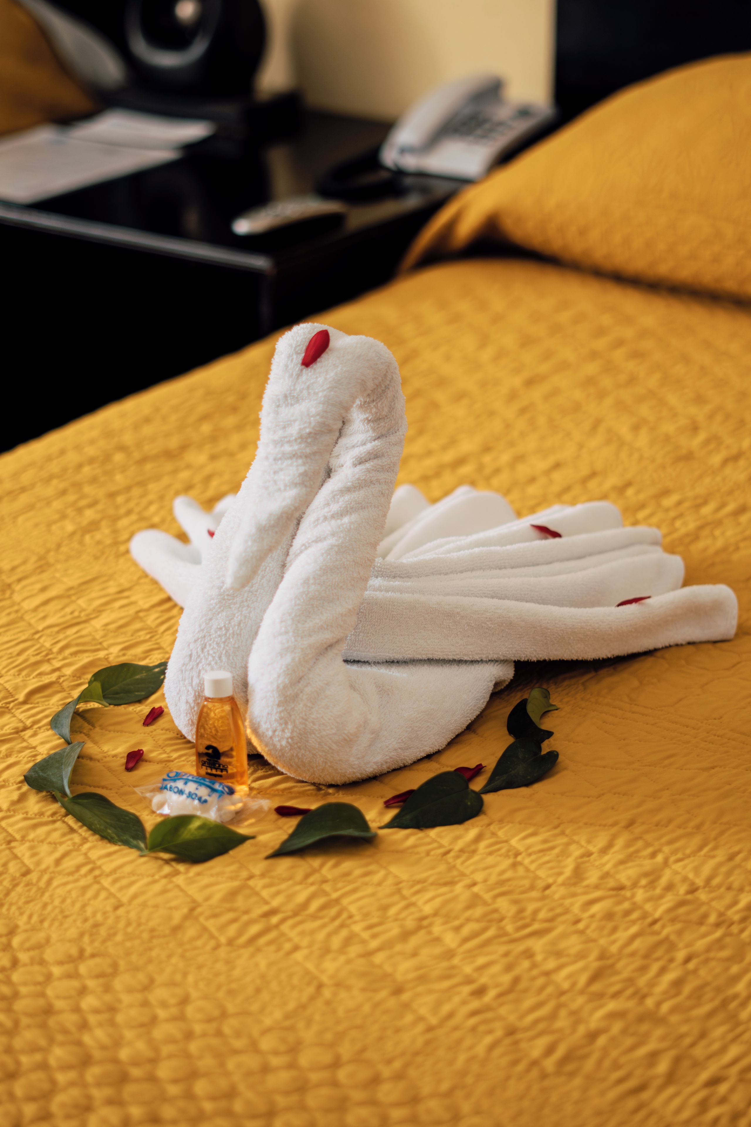 Una cama con una toalla con forma de cisne y una botella de loción.