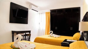 Una habitación de hotel con dos camas, un televisor montado en la pared, un escritorio y un armario.