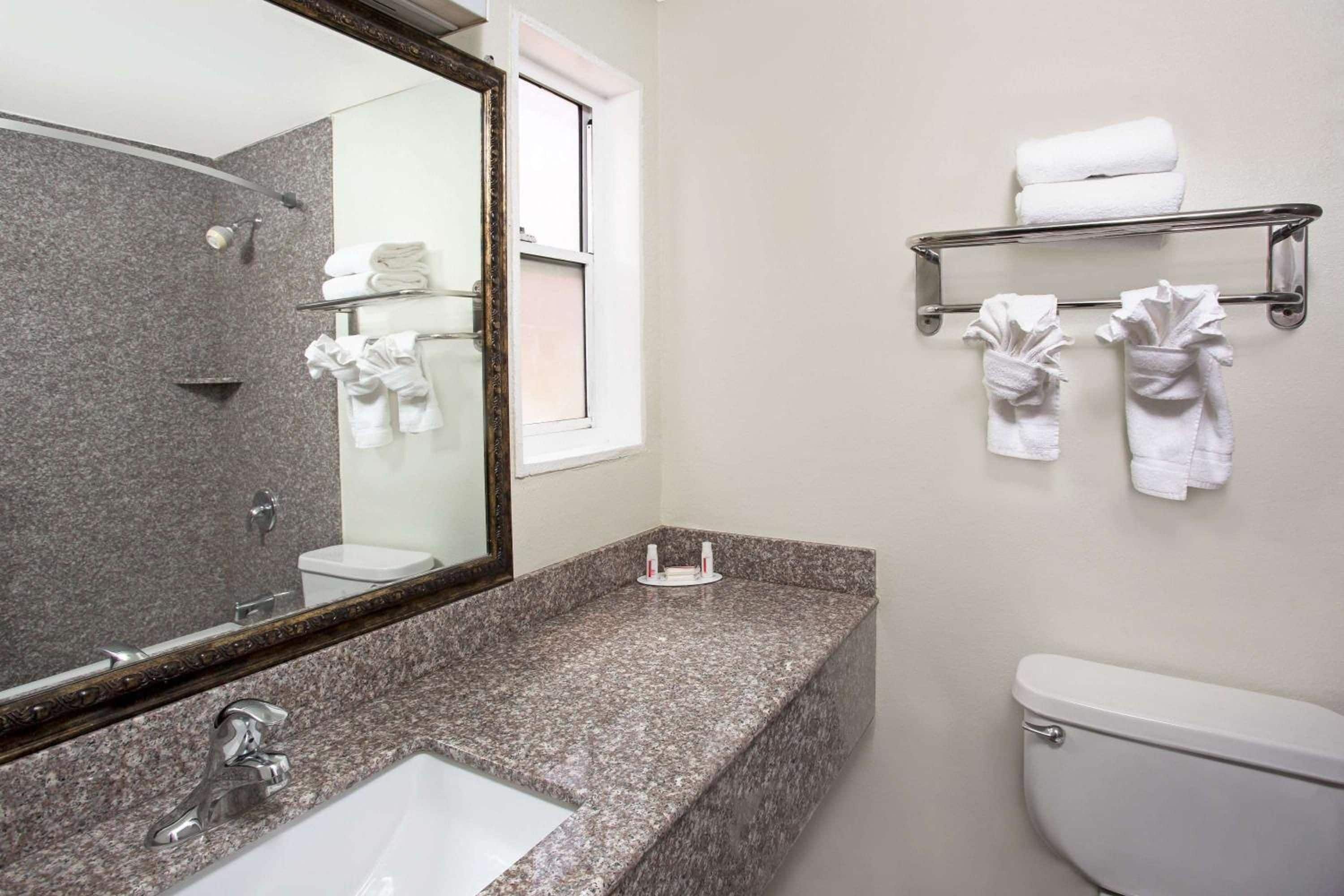A bathroom with a granite countertop, a sink, a toilet, a mirror, and towel racks.