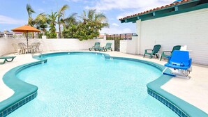 Une piscine dont le bord est recouvert de carrelage, entourée de chaises longues et bordée d’un mur blanc.