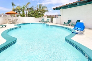 A swimming pool with a tiled edge, surrounded by lounge chairs and a white wall. - Sunset Inn (Costa Mesa)