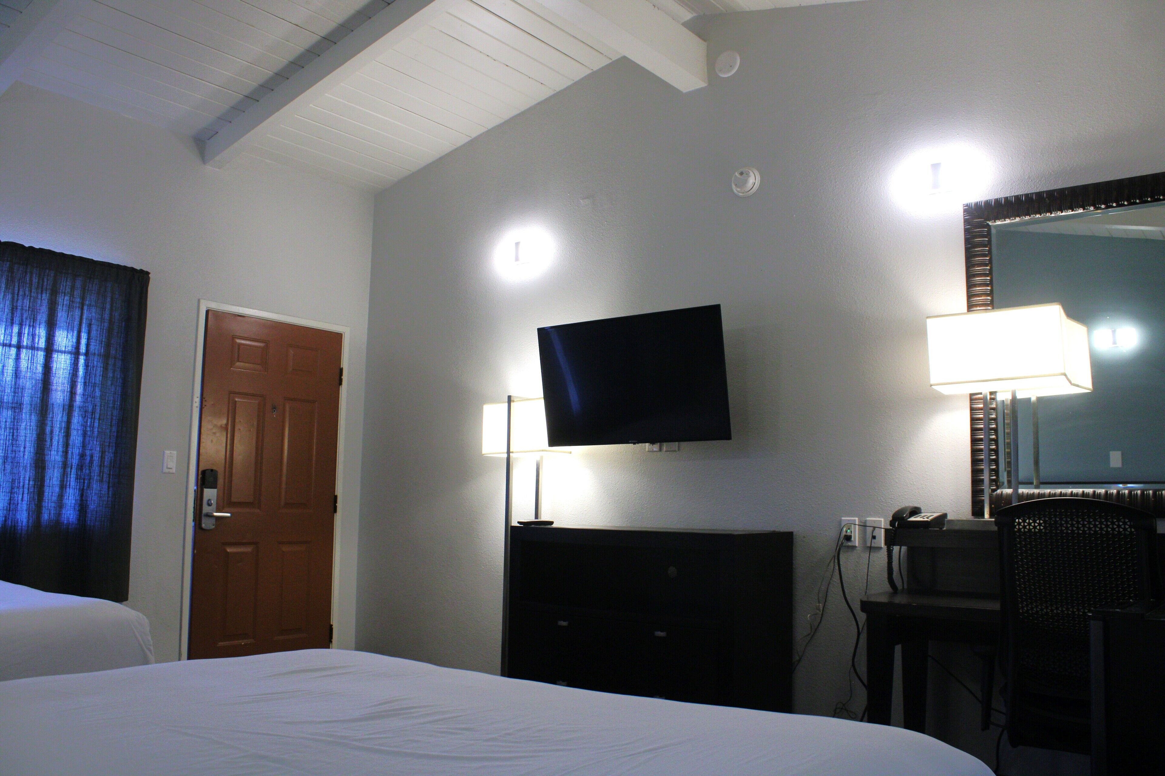 A hotel room with a bed, a television mounted on the wall, a desk with a chair, and a mirror.