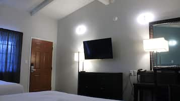 A hotel room with a bed, a television mounted on the wall, a desk with a chair, and a mirror.