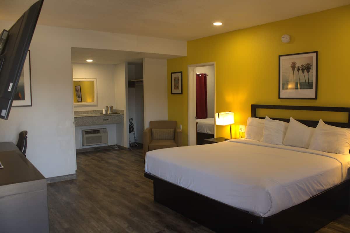 A hotel room with a large bed, a desk, a chair, and a kitchenette.