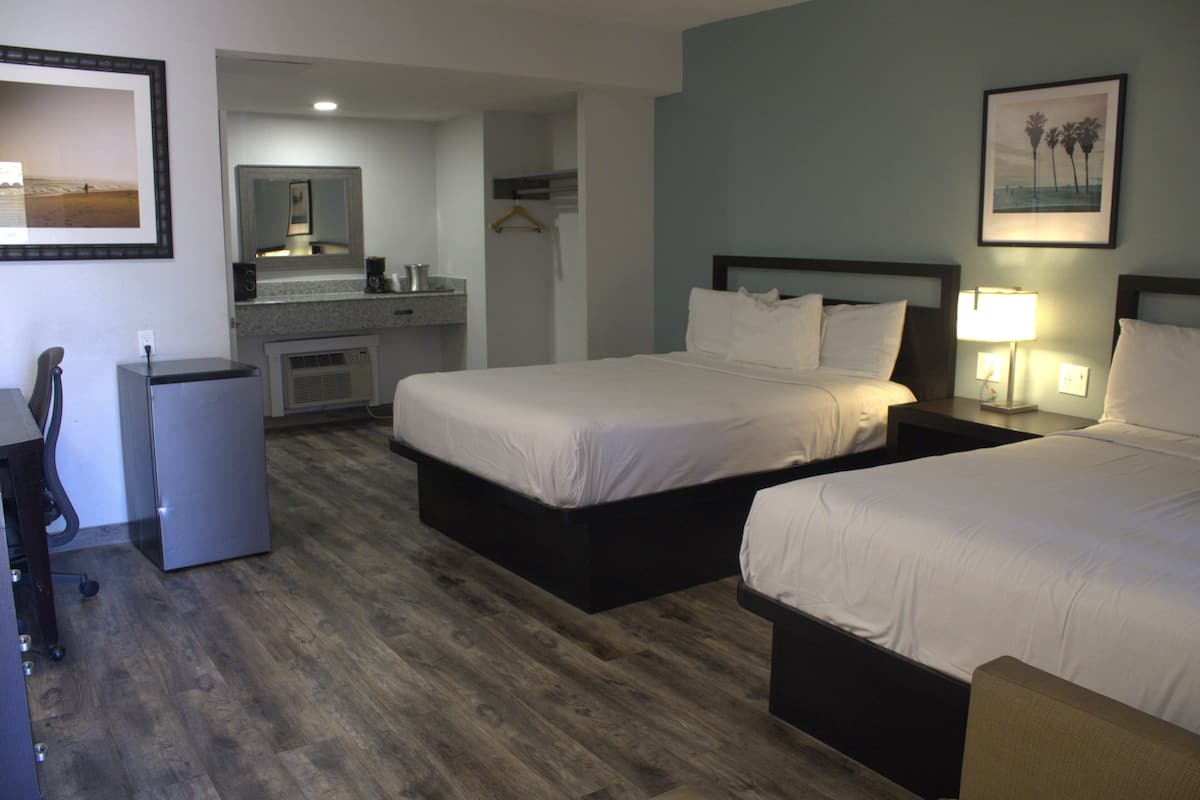 A hotel room with two beds, a small kitchenette, a mirror, and a framed picture on the wall.