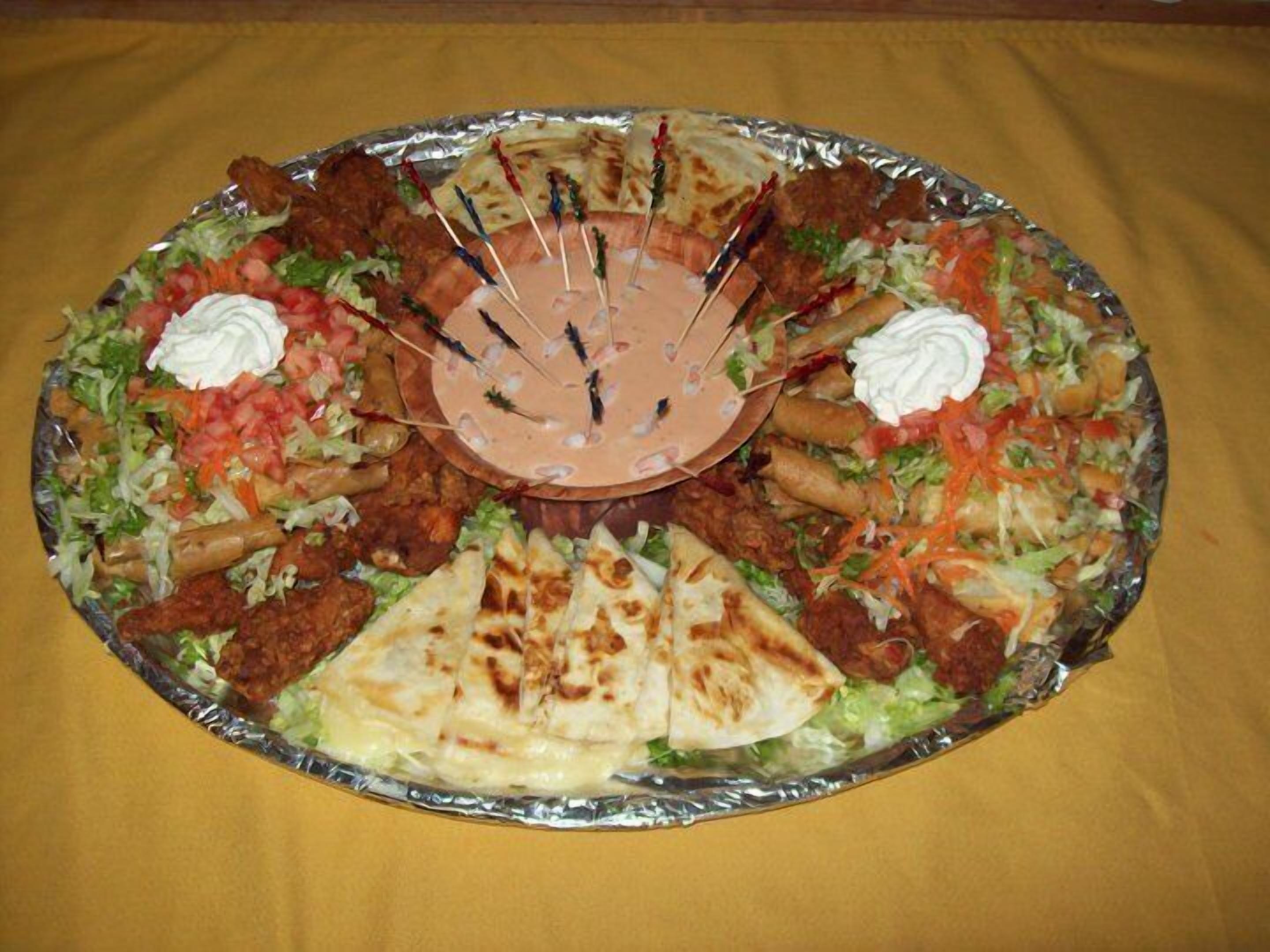 A large platter of various foods including tacos, grilled meats, and flatbreads, arranged on a foil-covered table.