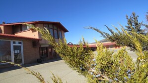 A building with a red roof and large windows, a paved area in front, and some greenery in the foreground.