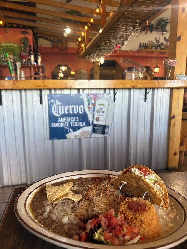 A restaurant interior with a bar area, a sign for Cuervo tequila, and a plate of food including beans, rice, and a taco.