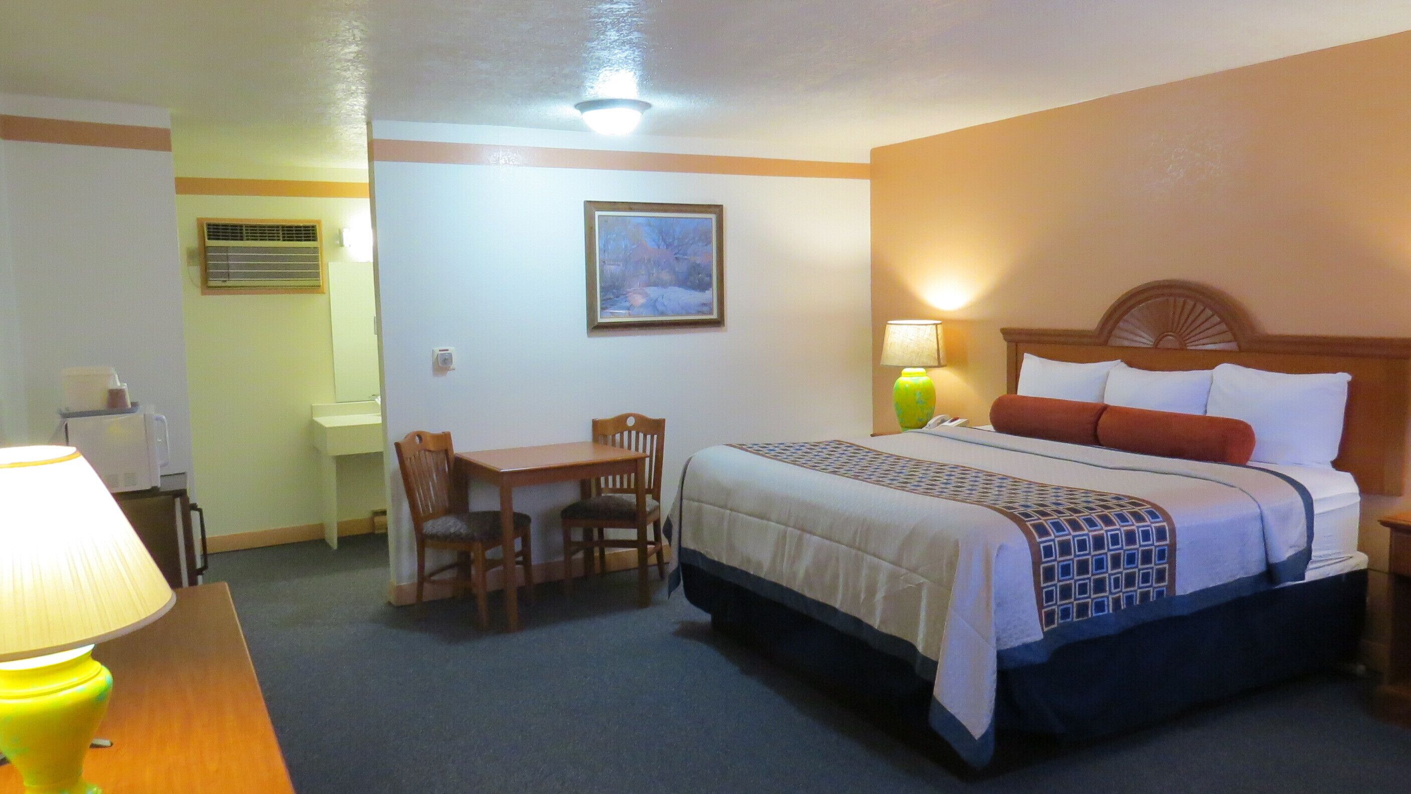 A hotel room with a bed, a desk, a chair, a lamp, and a painting on the wall.