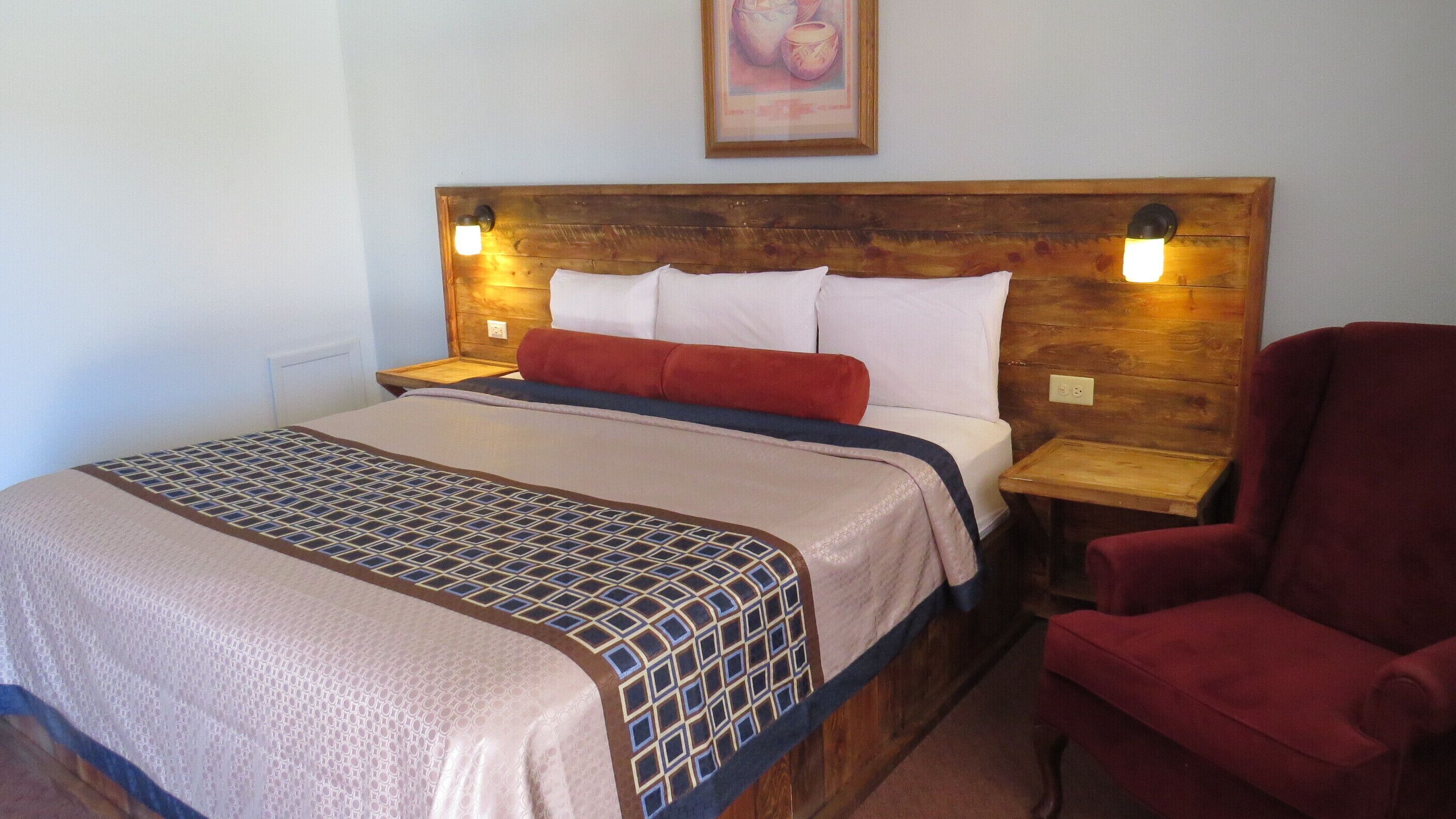 Un lit avec une couvre-lit à motifs, une tête de lit en bois, deux lampes de chevet et une chaise rouge.