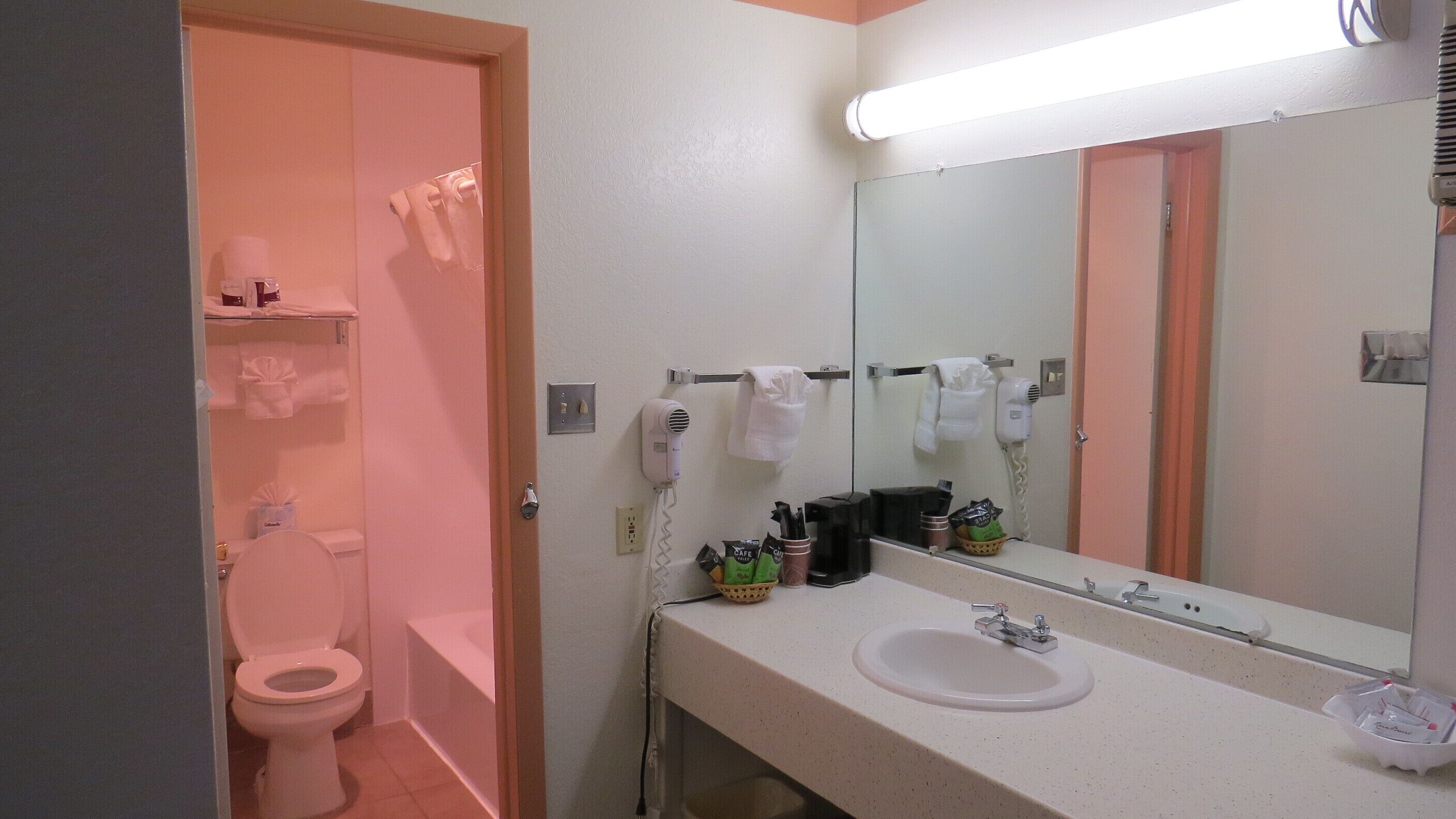 Baño con inodoro, lavabo y espejo. Hay secadores de pelo y un perchero para toallas.