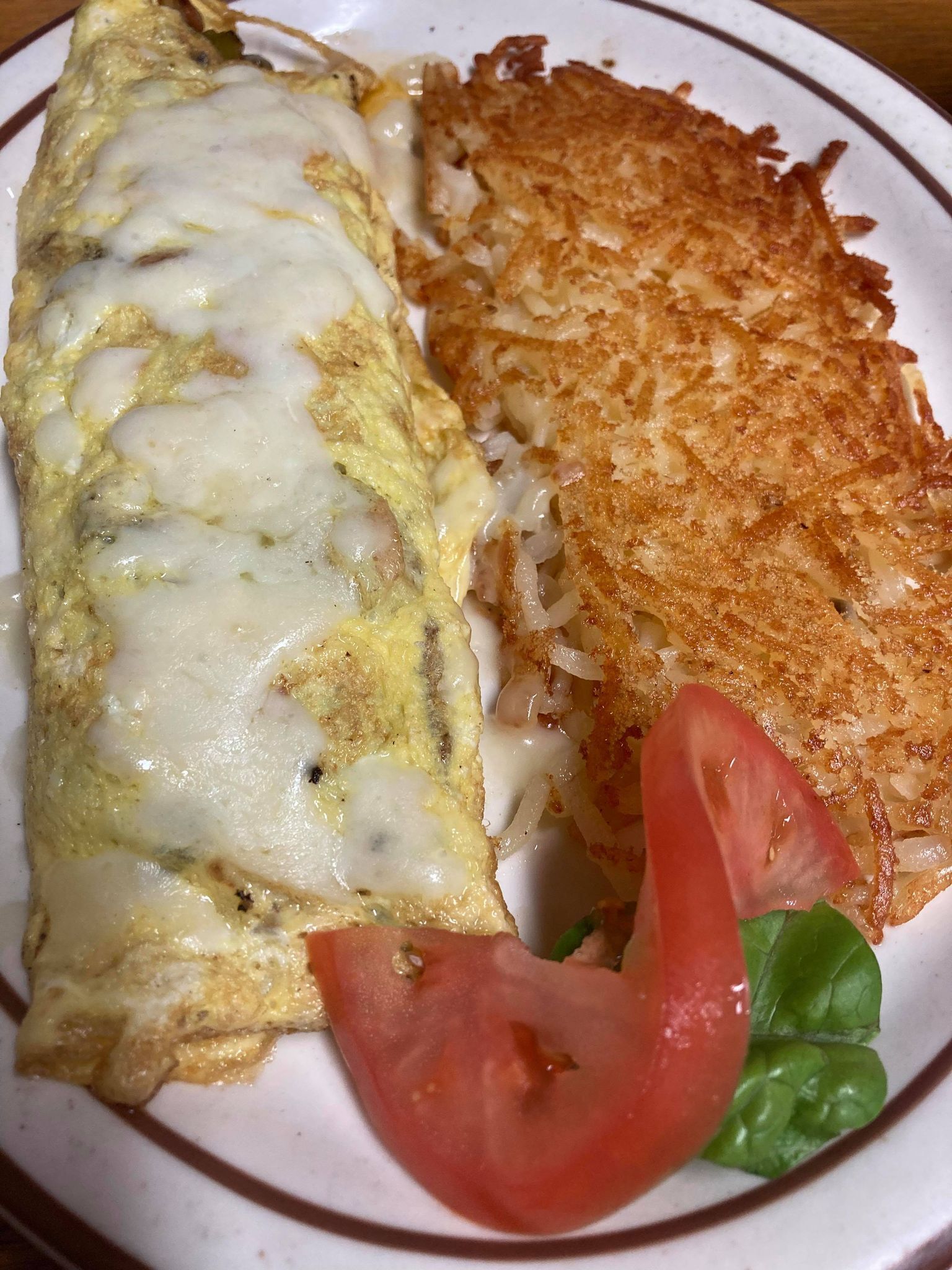 A plate with an omelette, hash browns, a slice of tomato, and a leaf of lettuce.