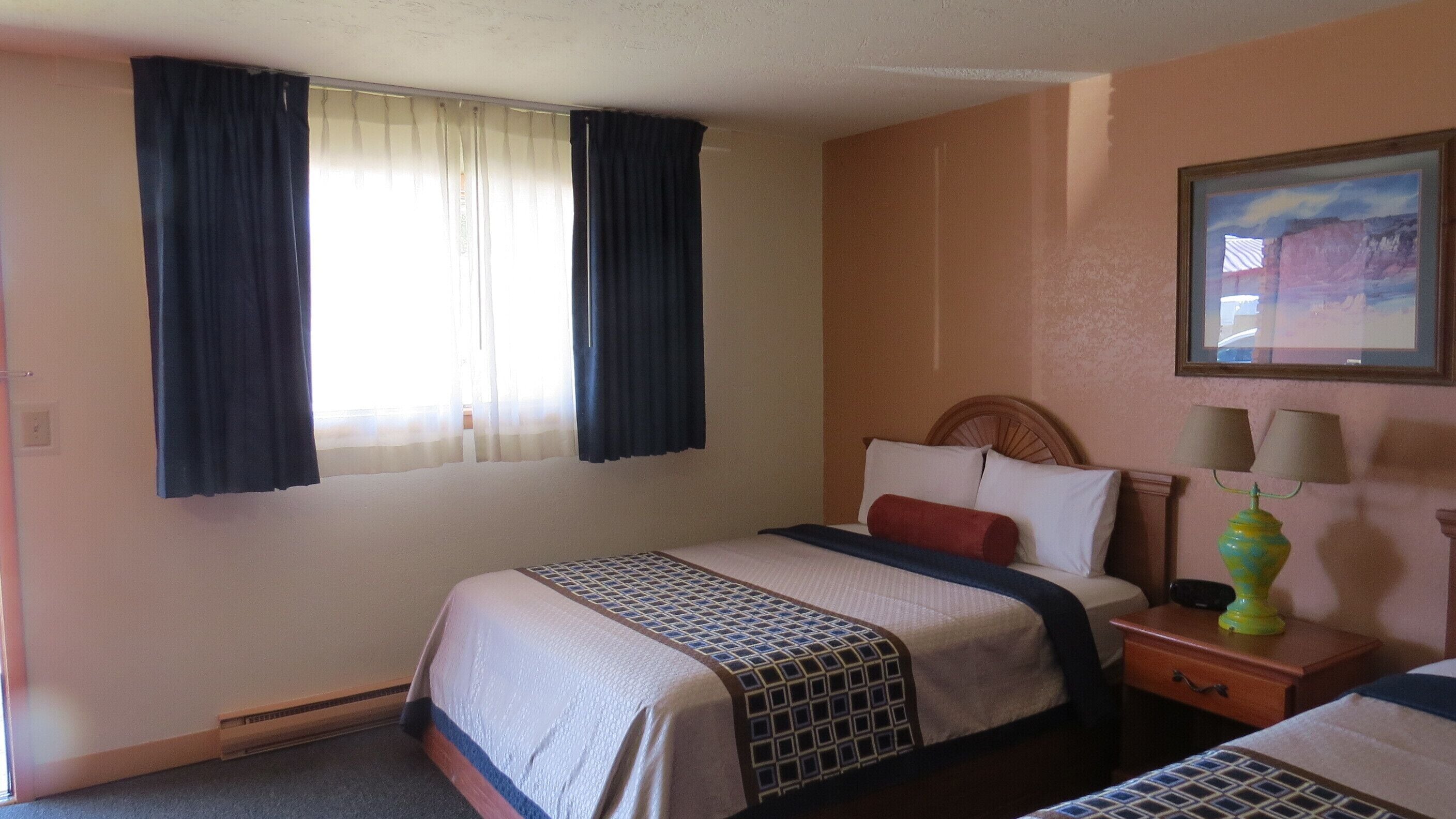 Quarto de hotel com cama, mesa de cabeceira, luminária e uma pintura na parede.