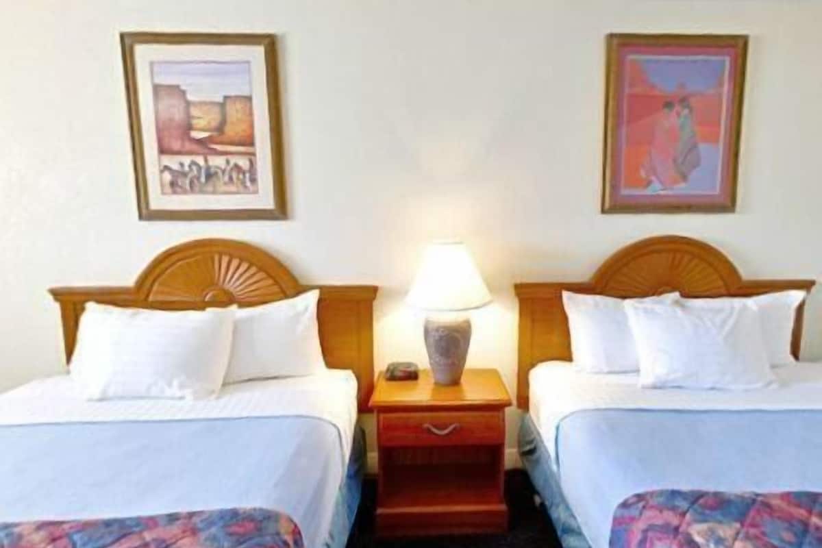 A hotel room with two beds, a nightstand with a lamp, and two framed pictures on the wall.