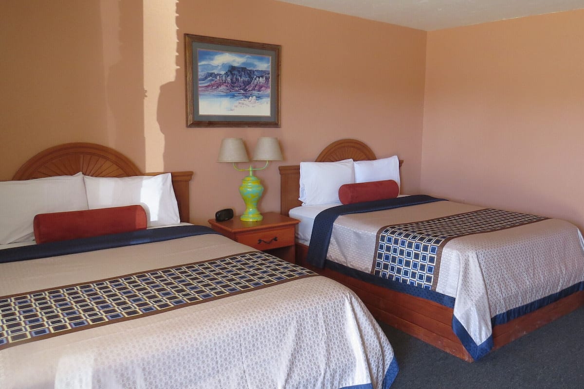 A hotel room with two beds, a nightstand with a lamp, and two framed pictures on the walls.