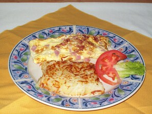 A plate with an omelette, hash browns, a slice of tomato, and a leaf of lettuce.