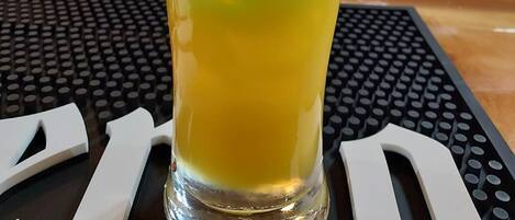 Un grand verre contenant un liquide dont la couleur dégrade du bleu au jaune, une paille jaune et une cerise rouge posée sur une tranche d’orange.