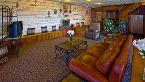 A spacious living room with a leather sofa, a coffee table, and a fireplace. There is a stone wall with framed pictures and a wooden bench.