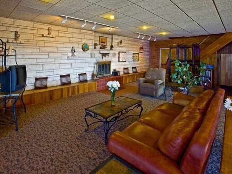 Un salon spacieux avec un canapé en cuir, une table basse et une cheminée. Un mur en pierre est décoré de tableaux encadrés, et un banc en bois y est adossé.