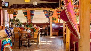 A restaurant with colorful tablecloths, wooden furniture, and a TV in the background.