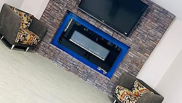 A room with a flat-screen TV mounted on a stone-patterned wall, two patterned armchairs, and a blue-framed fireplace.