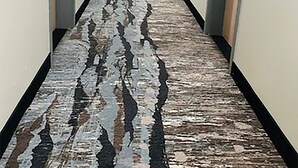 Un pasillo largo y estrecho con puertas a ambos lados, que conduce a habitaciones. El piso presenta un diseño con motivos.