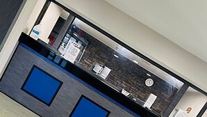 Un mostrador de recepción con una superficie oscura y tres paneles azules, un reloj y una ventana al fondo.