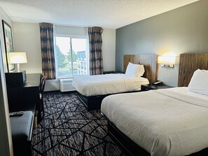A hotel room with two beds, a desk with a lamp, a chair, and a view of the outdoors. - BlissPoint Inn Northwest Indianapolis (Indianapolis)