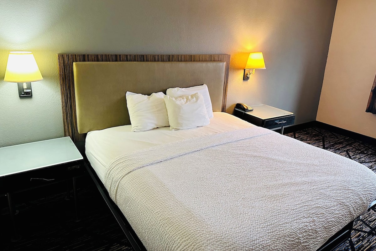 Una camera d'albergo con un letto, due comodini, una lampada e un telefono.